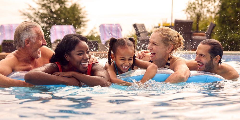 Smiling Multi-Generation Family On Summer Holiday Relaxing In Swimming Pool On Airbed
